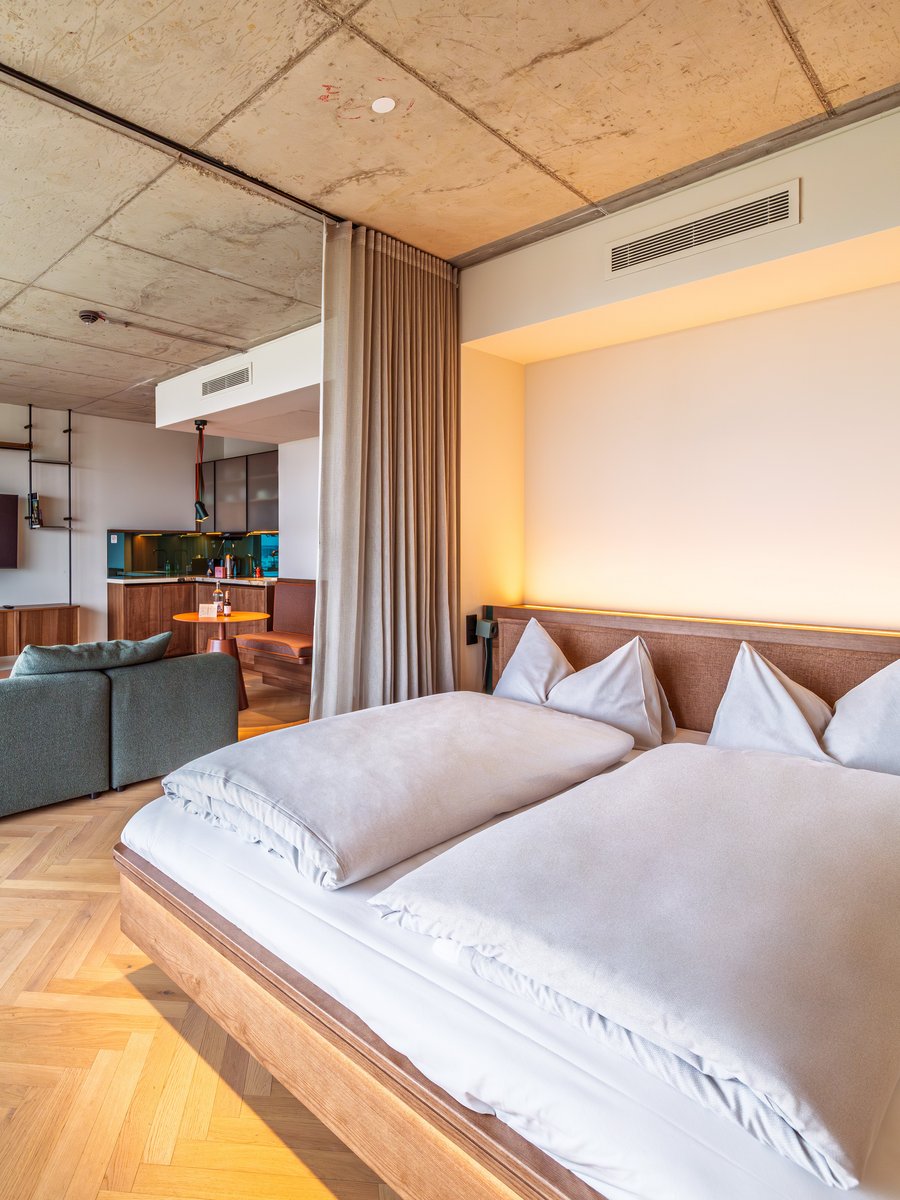 Blick über das Doppelbett in das großzügige Apartment Home mit angrenzendem Wohnbereich im The Zipper Hotel.