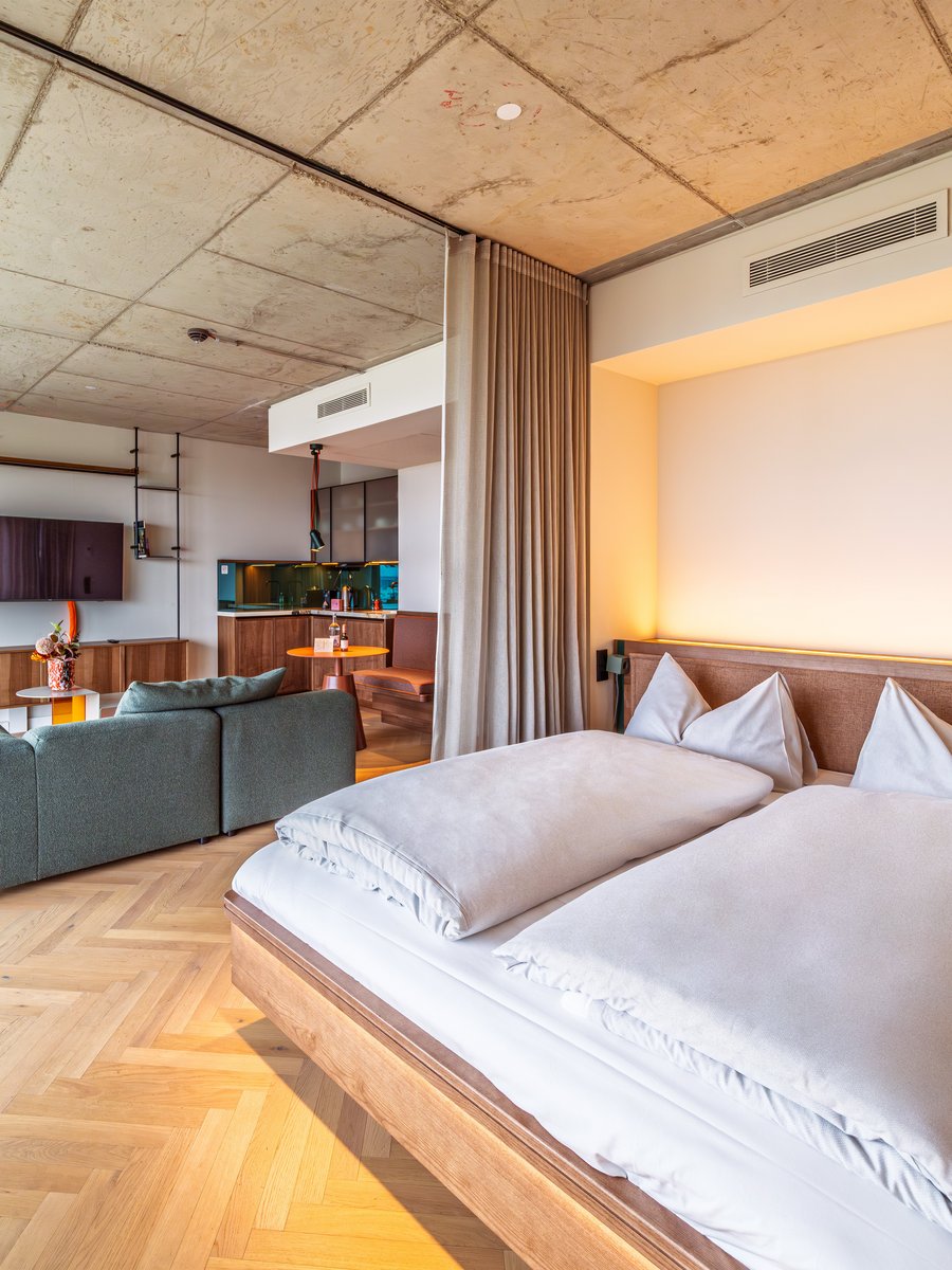 Blick über das Doppelbett in das großzügige Apartment Home mit angrenzendem Wohnbereich im The Zipper Hotel.
