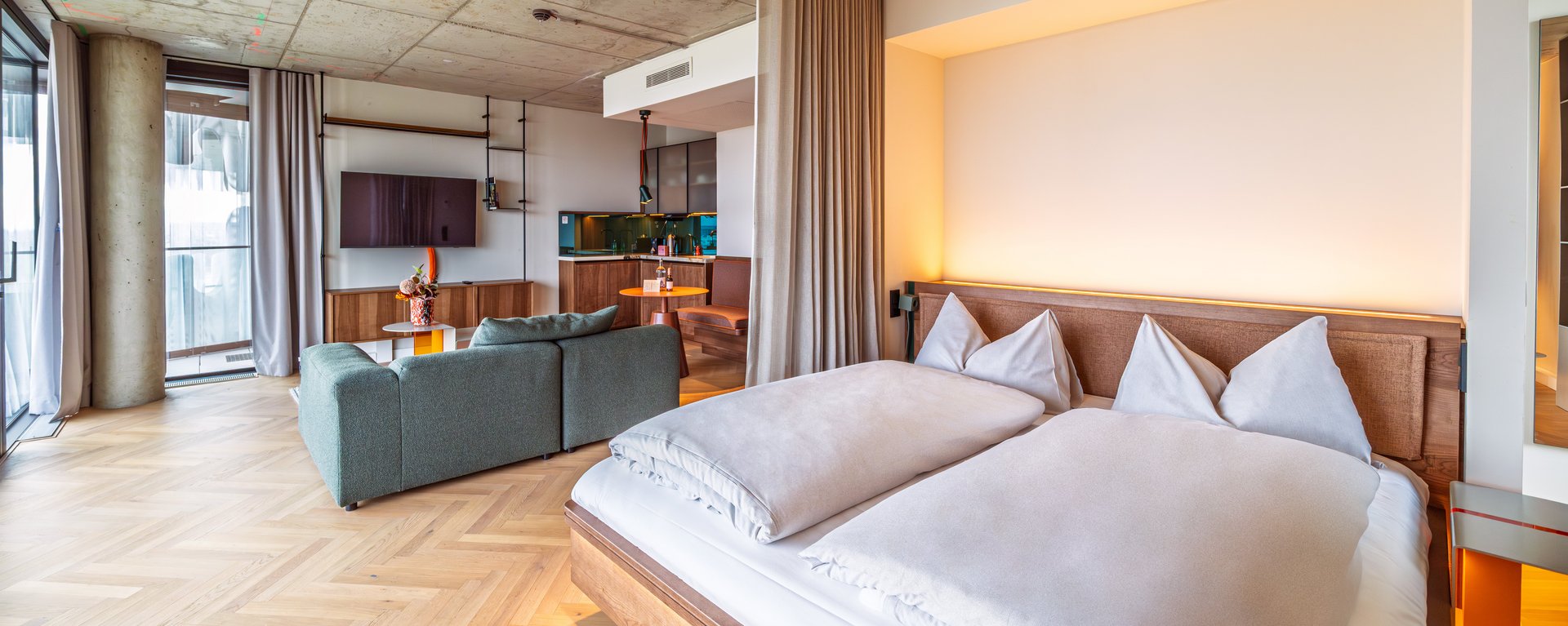 Blick über das Doppelbett in das großzügige Apartment Home mit angrenzendem Wohnbereich im The Zipper Hotel.