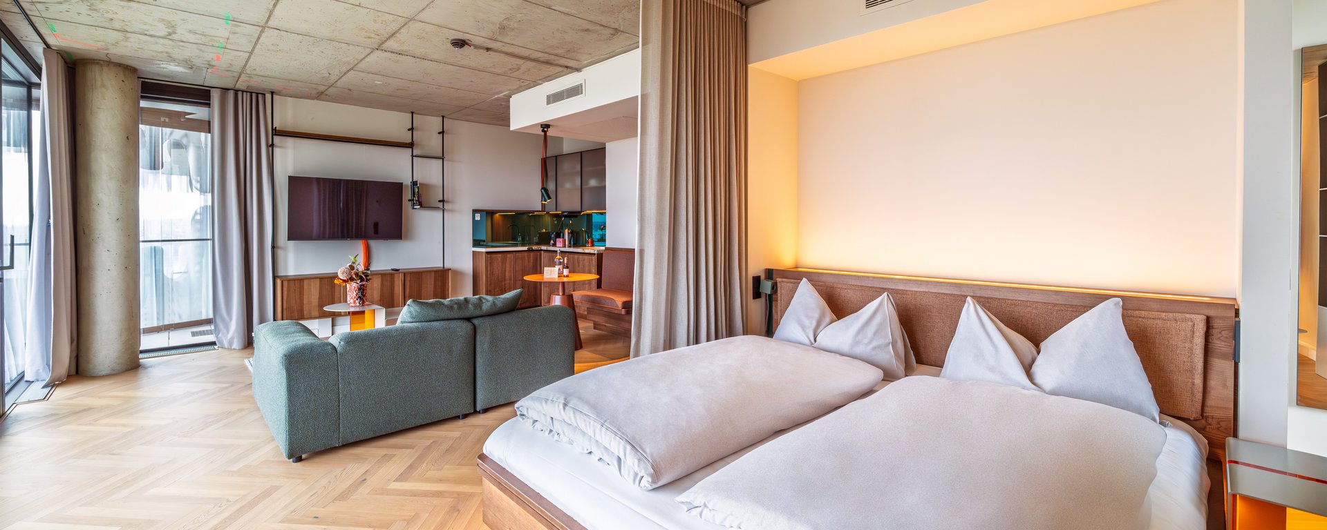 Blick über das Doppelbett in das großzügige Apartment Home mit angrenzendem Wohnbereich im The Zipper Hotel.