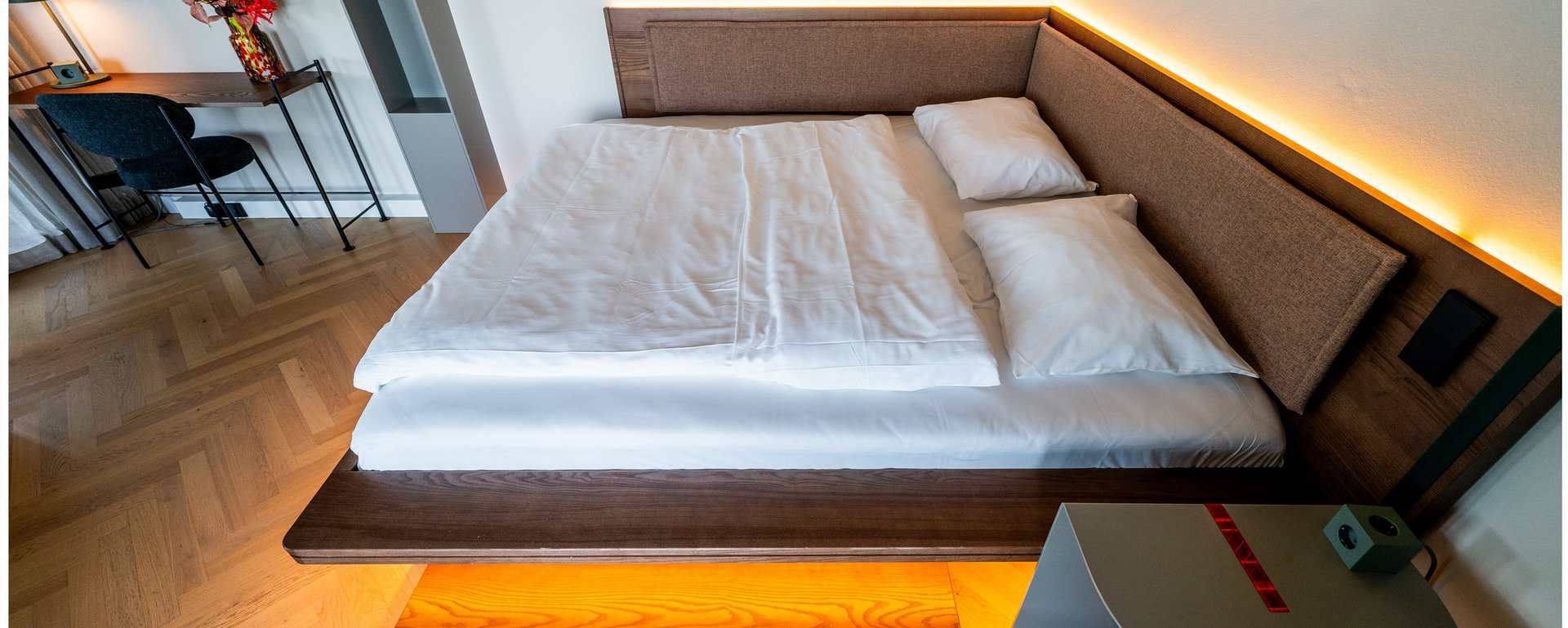 Hotelzimmer mit großem Doppelbett, modernem Nachttisch und LED-Beleuchtung im THE ZIPPER Hotel Düsseldorf.