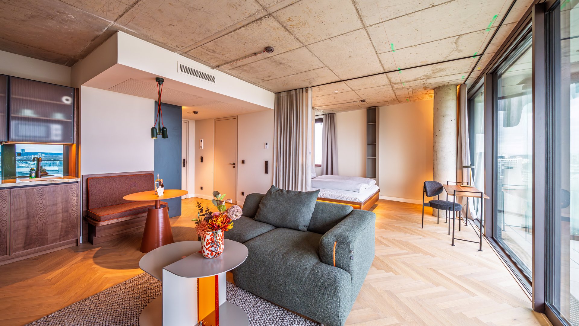 Gemütliche Sitzecke im Apartment Home mit grünem Sofa, Designtisch und großen Fensterfronten.