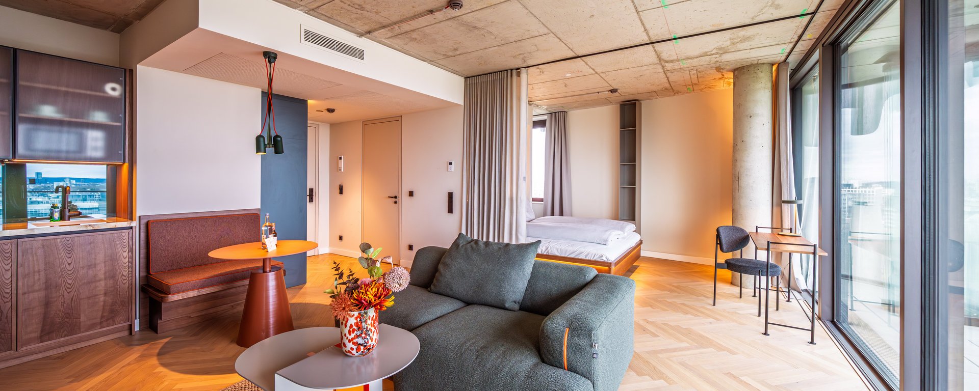 Gemütliche Sitzecke im Apartment Home mit grünem Sofa, Designtisch und großen Fensterfronten.