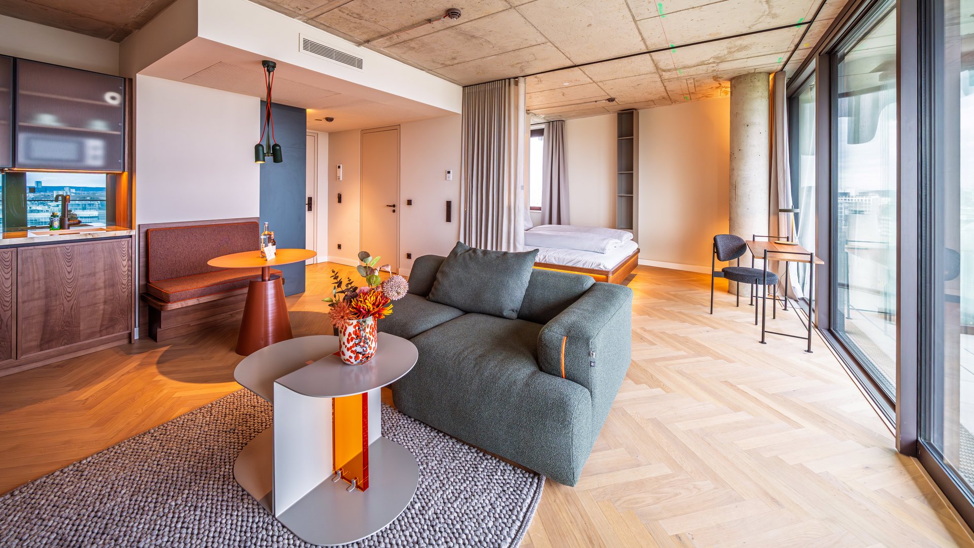 Gemütliche Sitzecke im Apartment Home mit grünem Sofa, Designtisch und großen Fensterfronten.