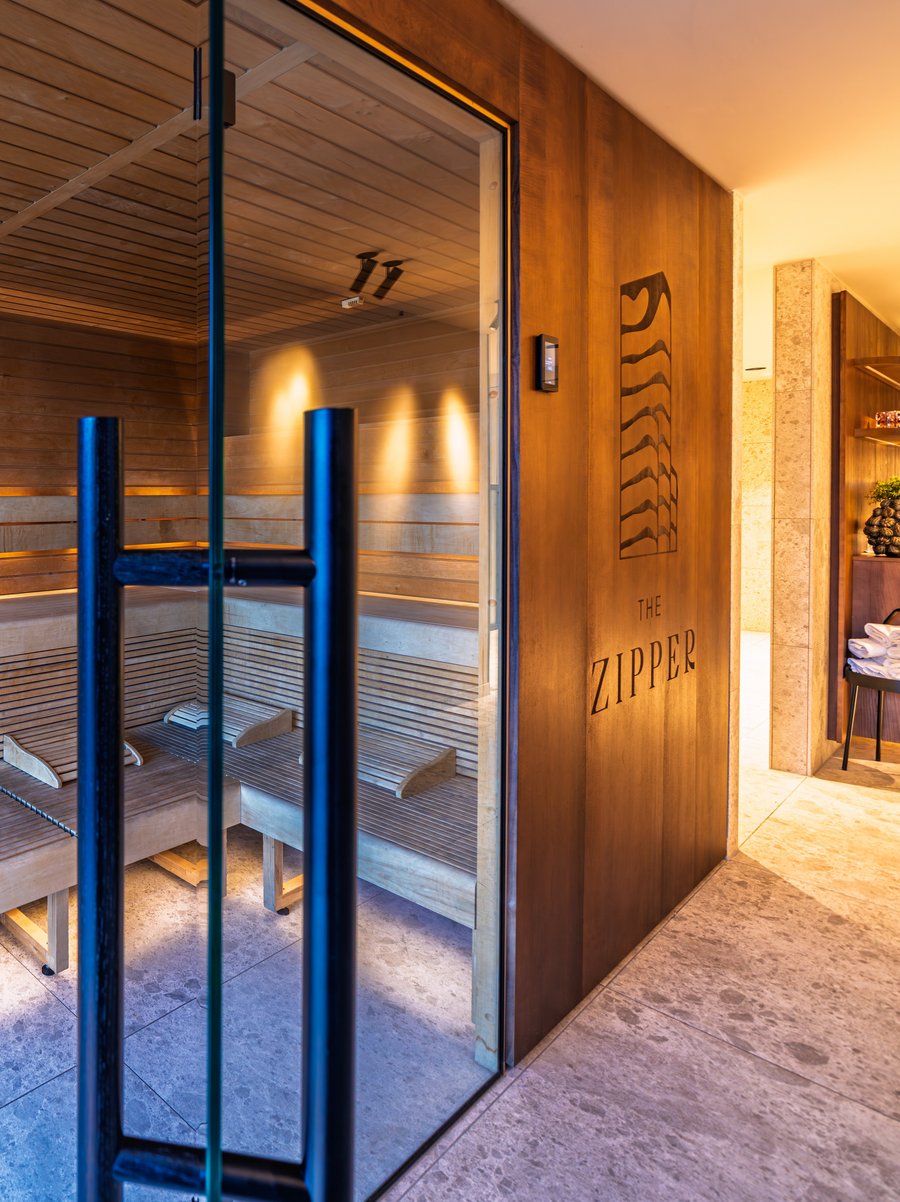 Moderne Holzsauna mit Glasfront und indirekter Beleuchtung im Wellnessbereich des Hotels.