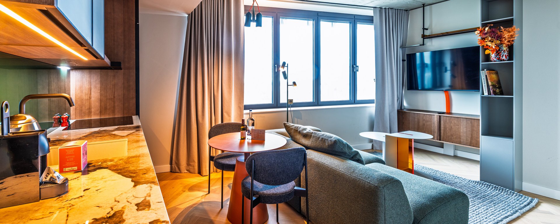 Wohnbereich der Suite mit grünem Sofa, Esstisch und moderner Küchenzeile in Holzoptik.