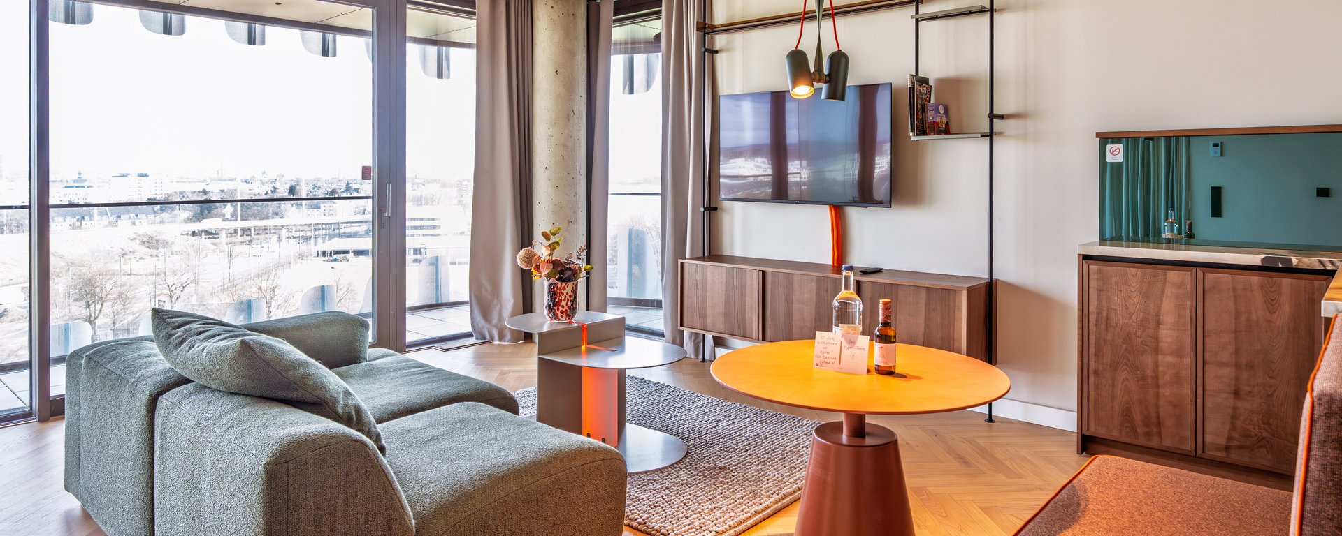 Wohnbereich im Apartment Home mit Blick auf die Fensterfront und minimalistisches Interieur.