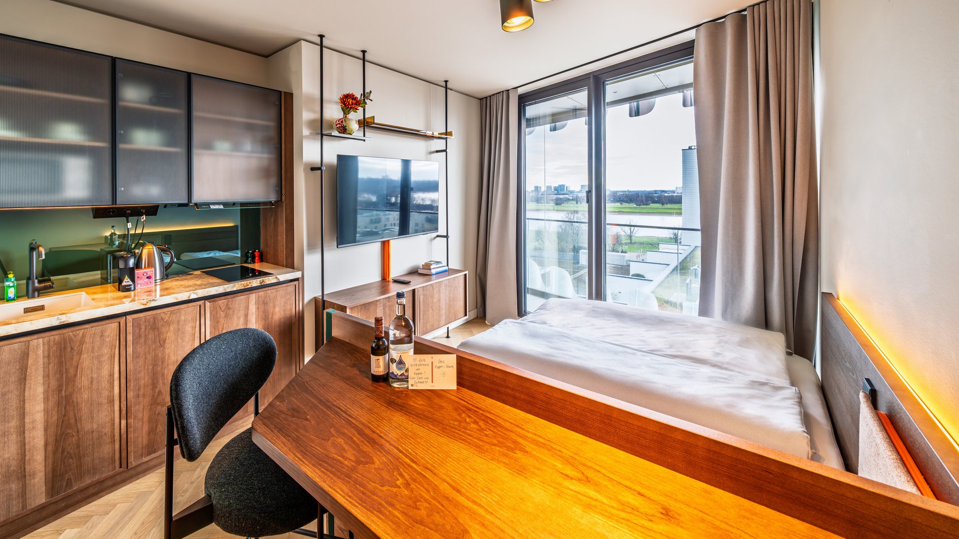 Modernes Apartment im The Zipper Hotel mit Holztisch, Kochnische und Blick auf das Bett sowie ein großes Fenster.