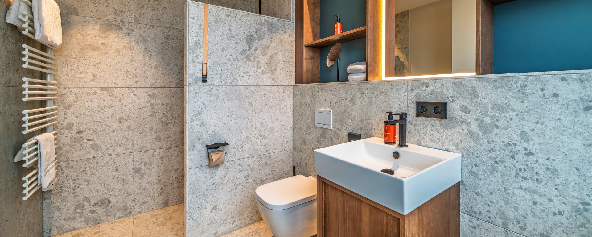 Großzügiges Badezimmer in der Suite mit dunklem Holzwaschtisch, großem Spiegel und hellen Fliesen.