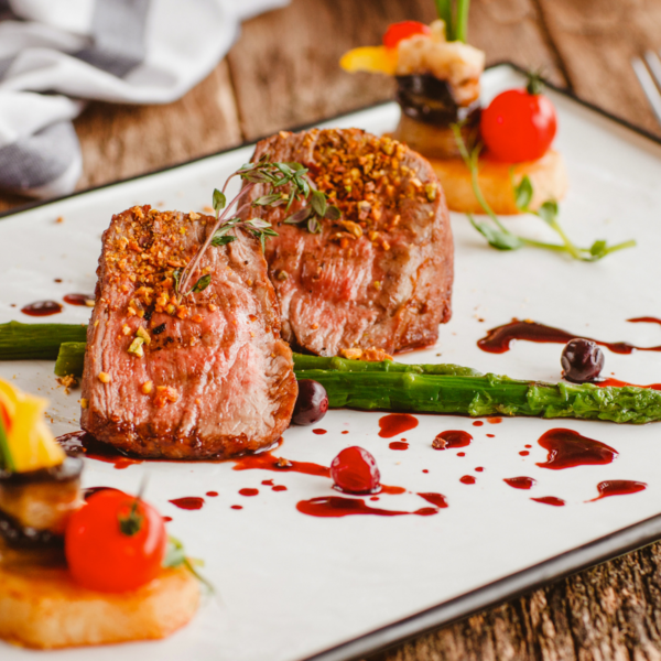 Gourmetgericht mit Fleisch, grünem Spargel, Tomaten und feiner Garnitur auf elegantem Teller angerichtet.