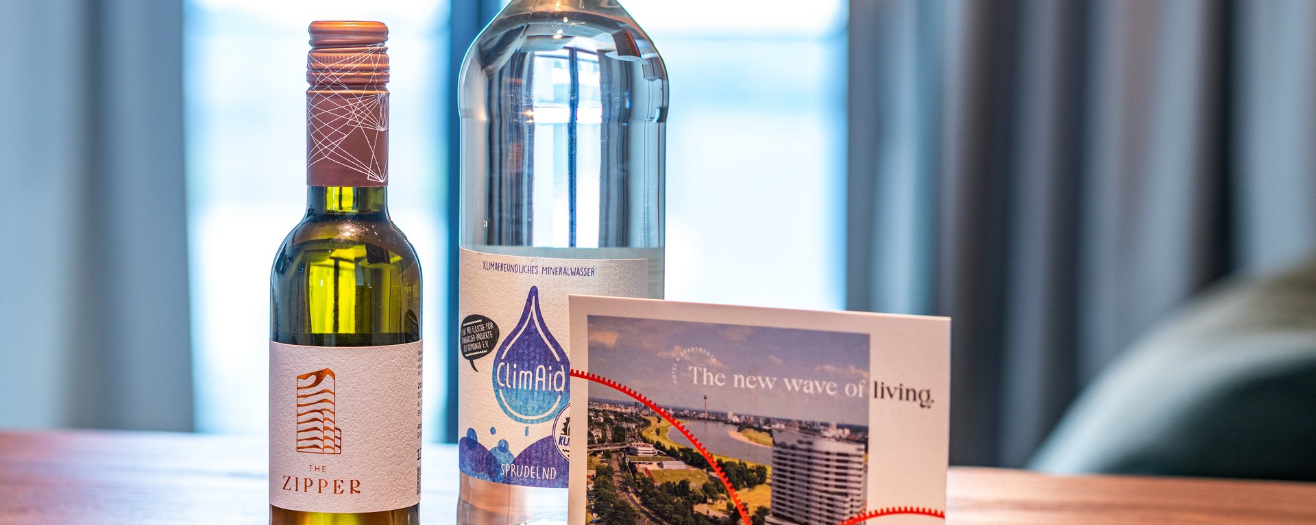 Willkommens-Set auf dem Holztisch der Suite mit Wasser, Wein und einer persönlichen Grußkarte.