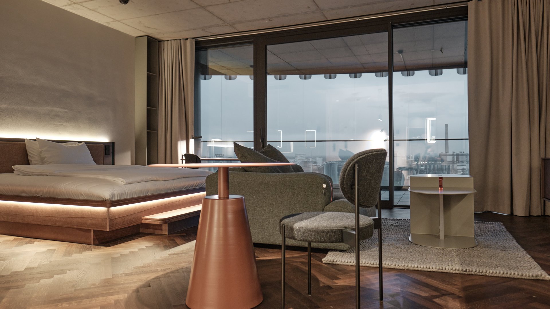 Apartment im The Zipper Düsseldorf mit Doppelbett, Lounge-Bereich, Designmöbeln und bodentiefen Fenstern mit Ausblick – ideal für Langzeitaufenthalte.