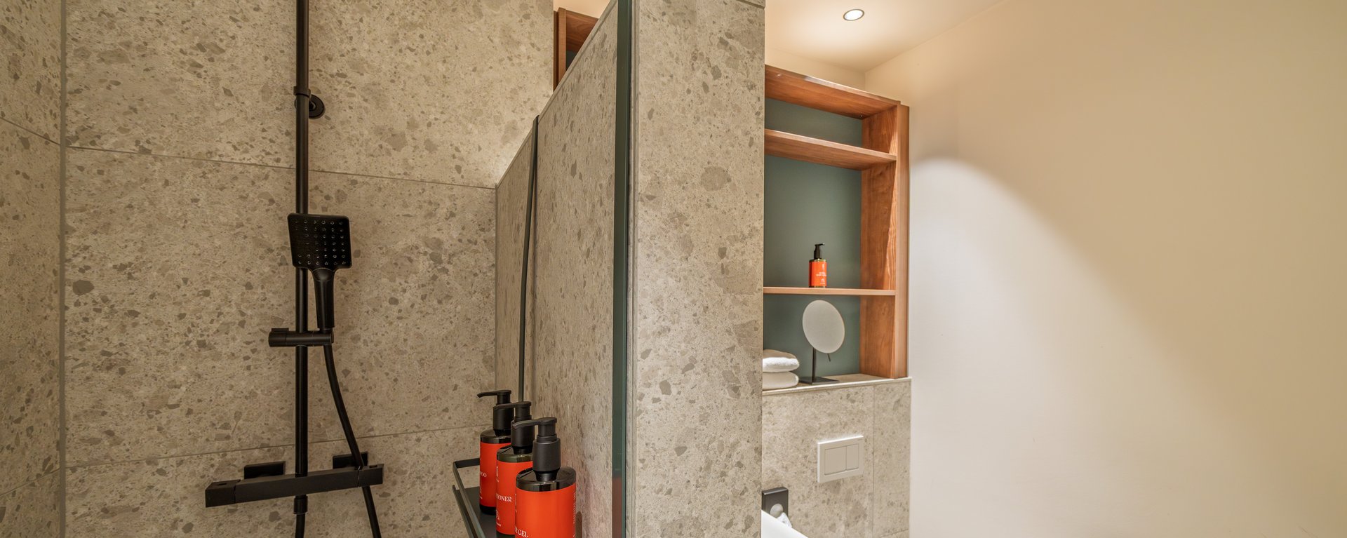 Helles Badezimmer im The Zipper Hotel Apartment mit moderner Regendusche, grauen Fliesen und Holzdetails.