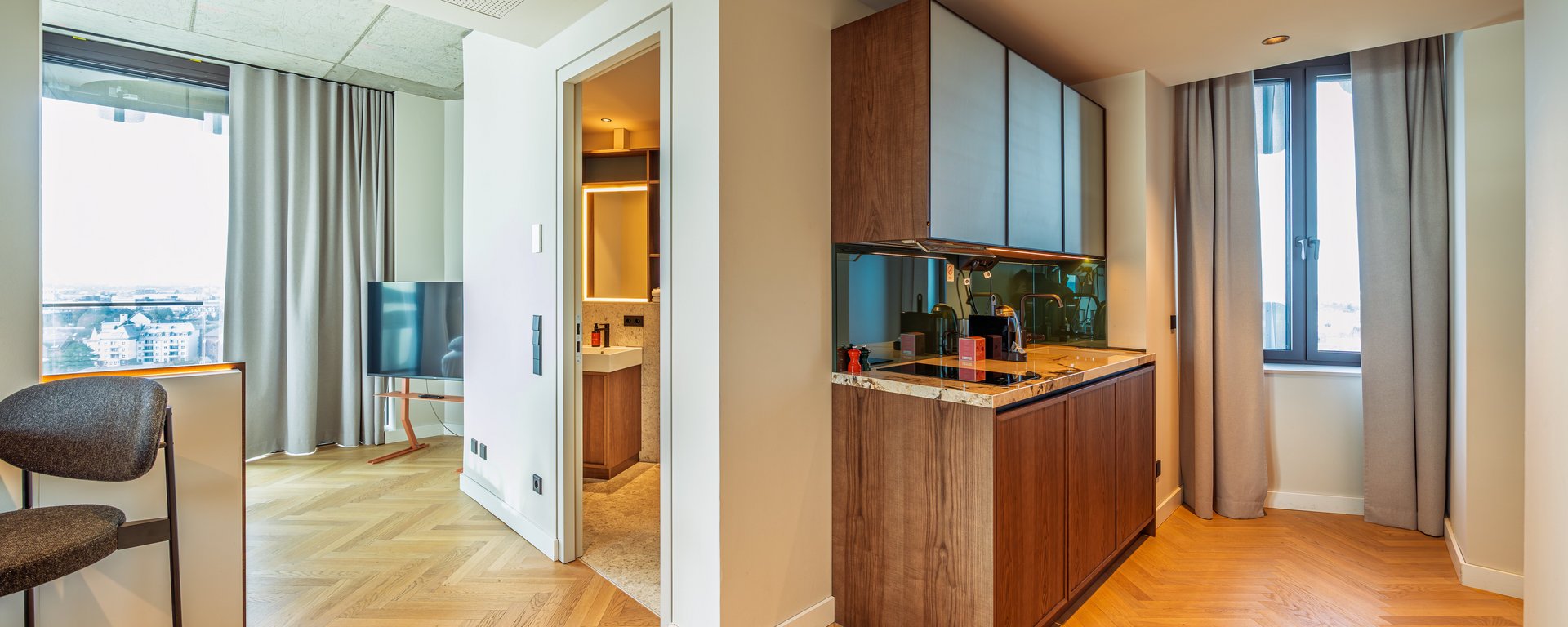 Eingangsbereich der Suite mit Blick auf die Küchenzeile, Parkettboden und den hellen Wohnraum.