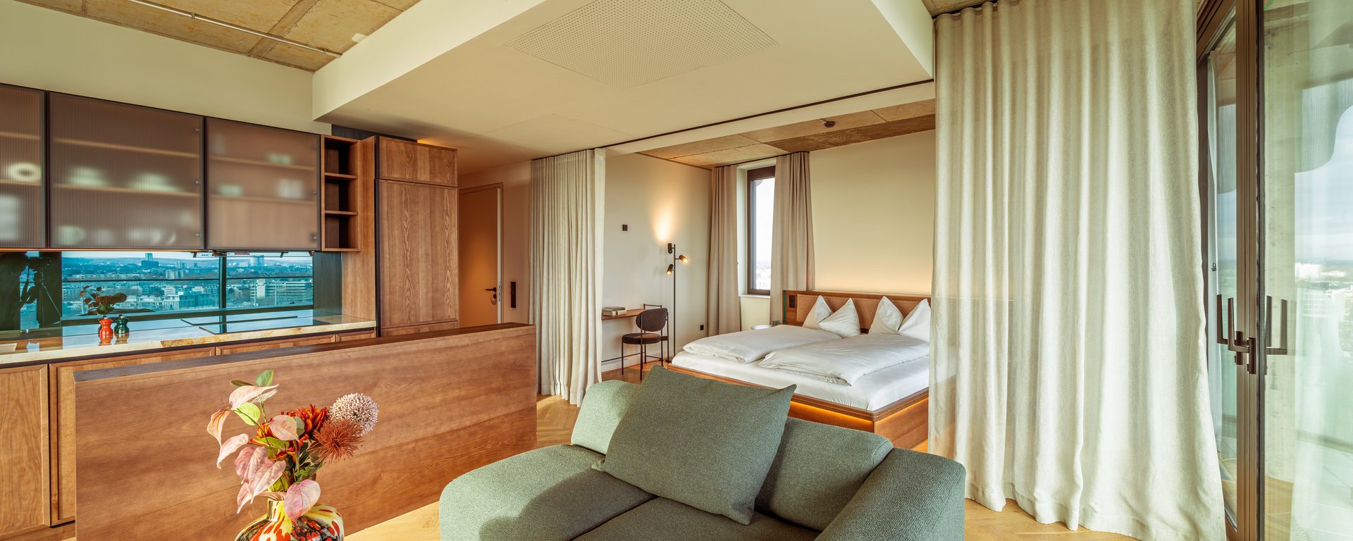 Gemütliches Wohnzimmer im Apartment Home Skyline mit grünem Sofa und Blick Richtung Schlafbereich.