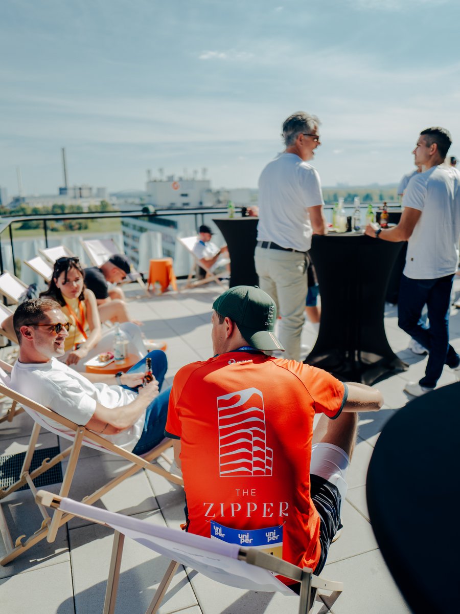 zipper_marathon__1_.jpg Gruppe von Menschen entspannt auf einer Rooftop-Terrasse in Düsseldorf mit Liegestühlen und Stehtischen.