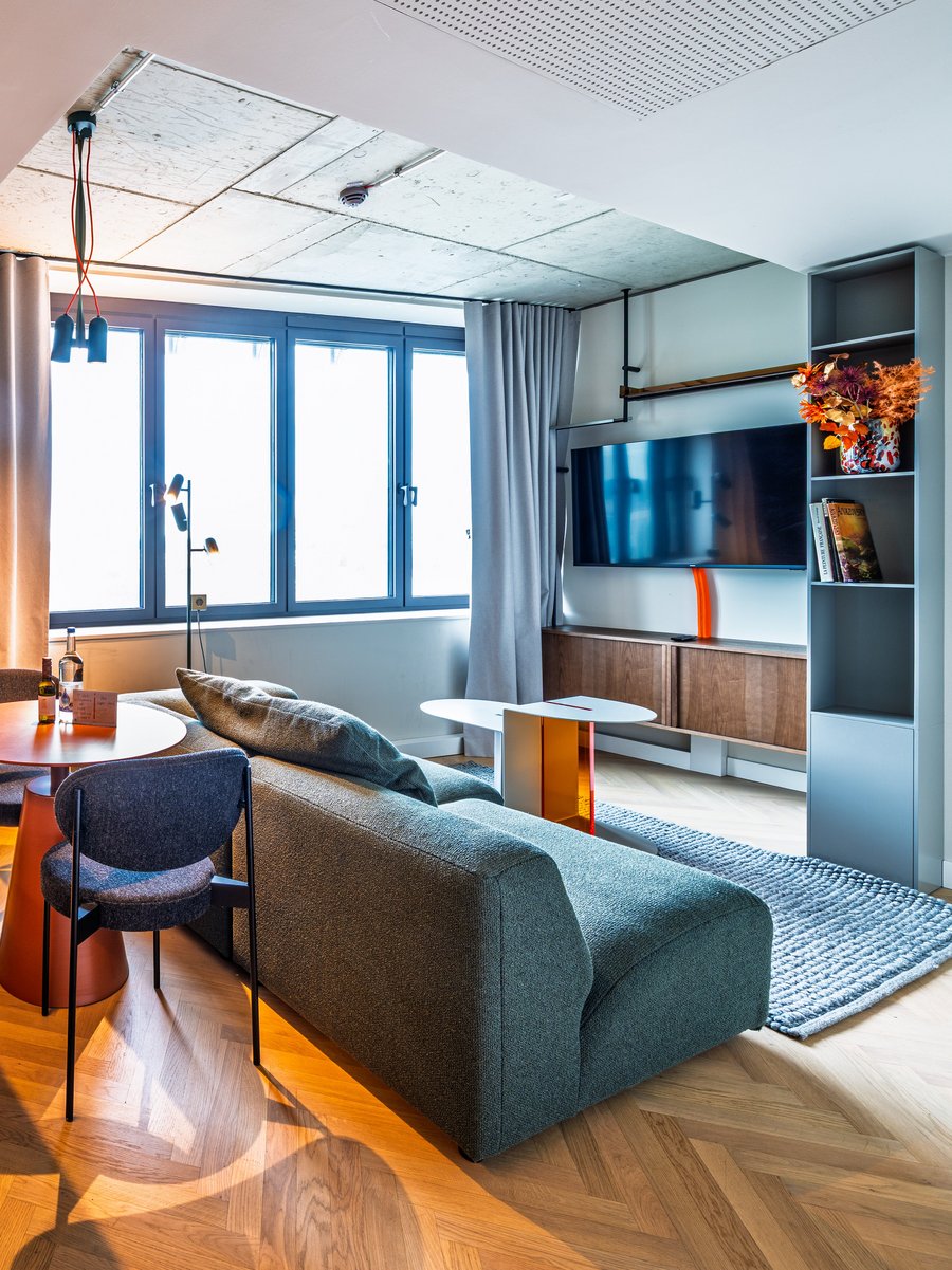 Wohnbereich der Suite mit grünem Sofa, Esstisch und moderner Küchenzeile in Holzoptik.