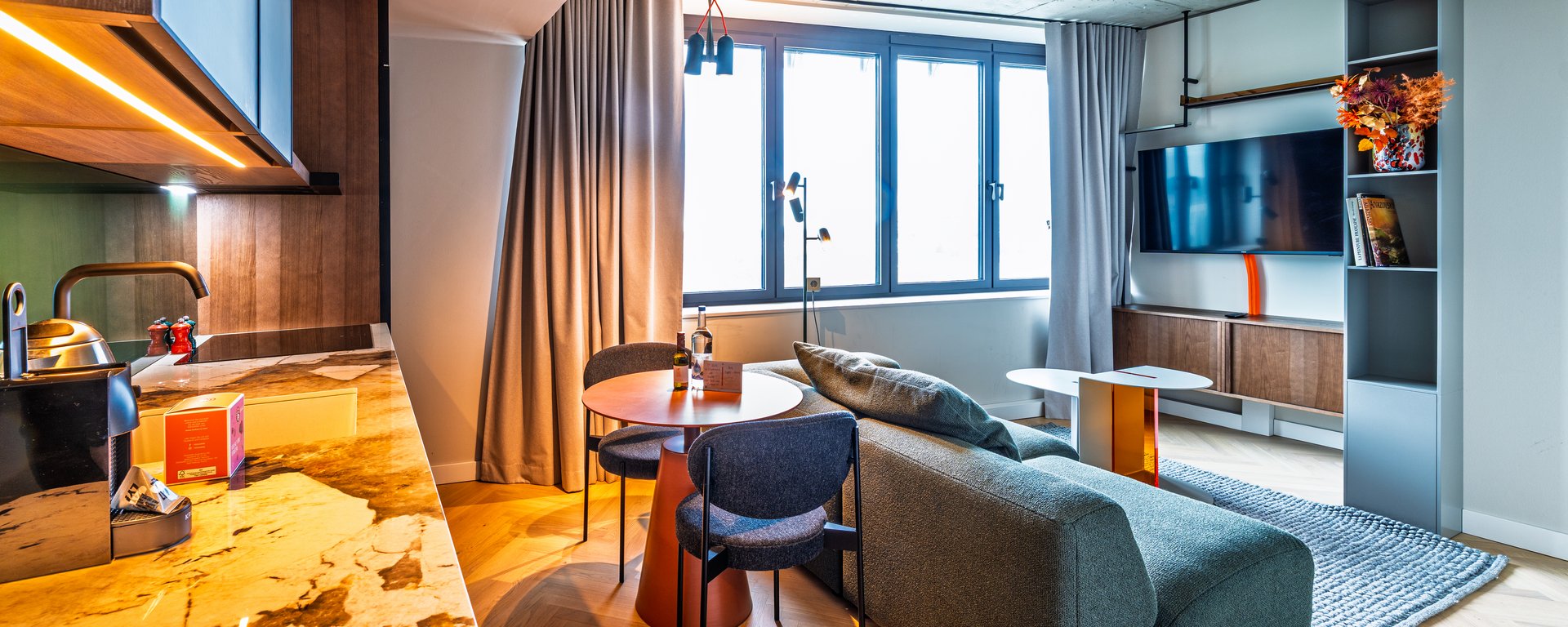 Wohnbereich der Suite mit grünem Sofa, Esstisch und moderner Küchenzeile in Holzoptik.