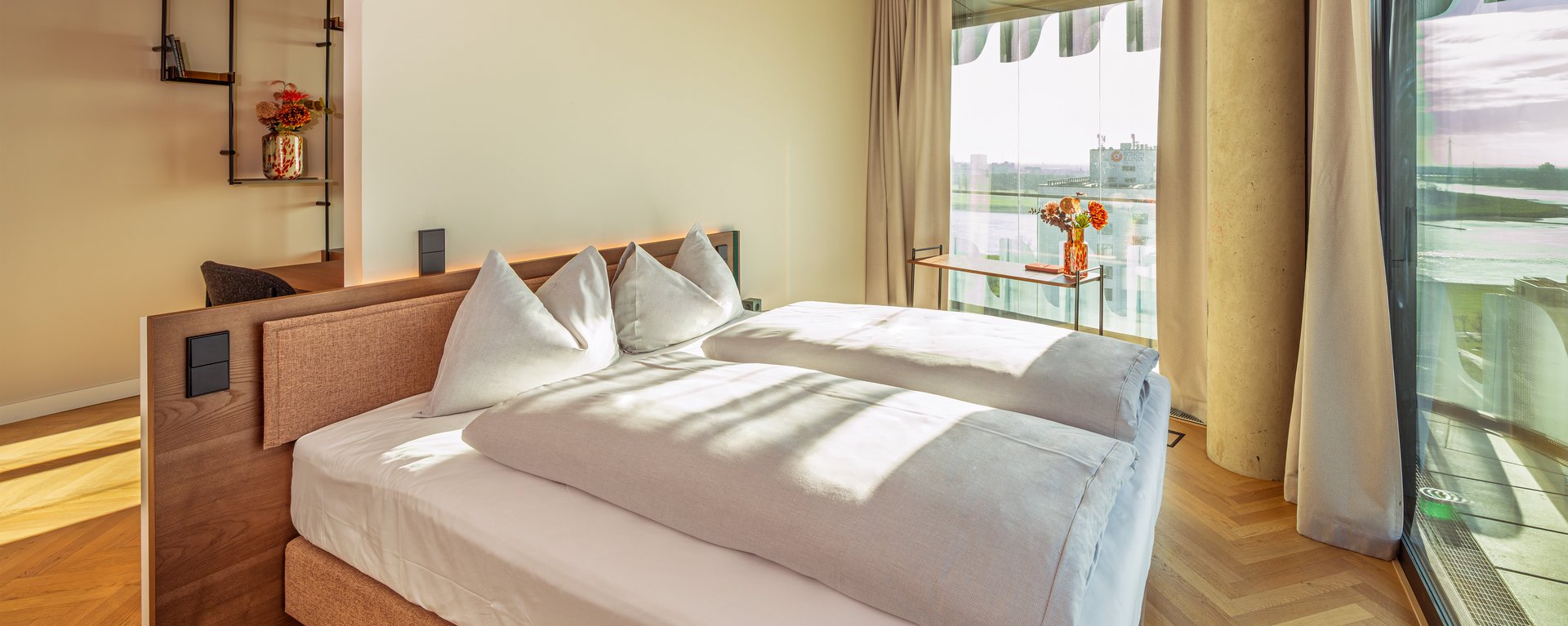 Schlafzimmer der Suite Loggia mit Doppelbett und bodentiefen Fenstern, die viel Tageslicht hereinlassen.