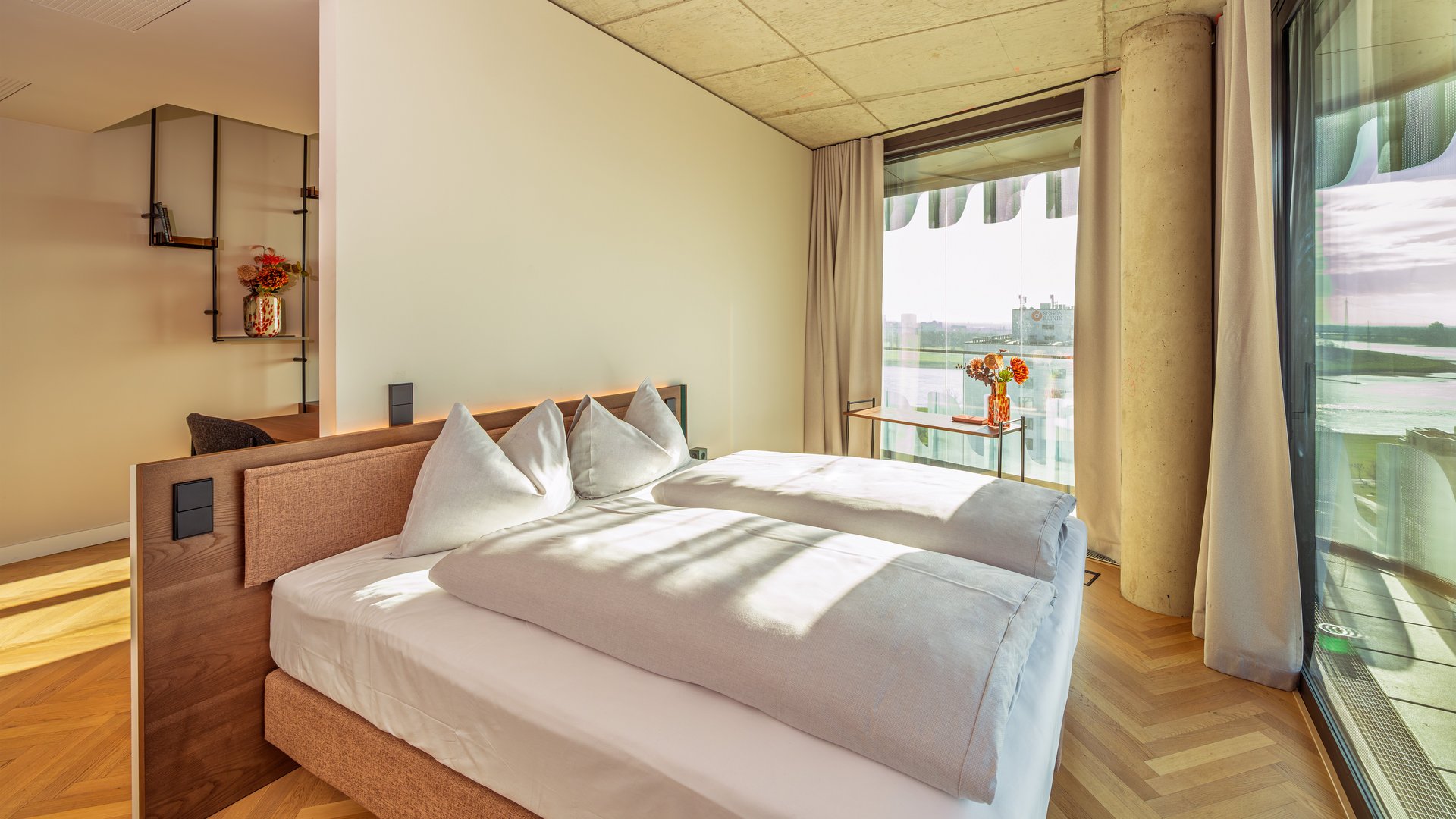 Schlafzimmer der Suite Loggia mit Doppelbett und bodentiefen Fenstern, die viel Tageslicht hereinlassen.