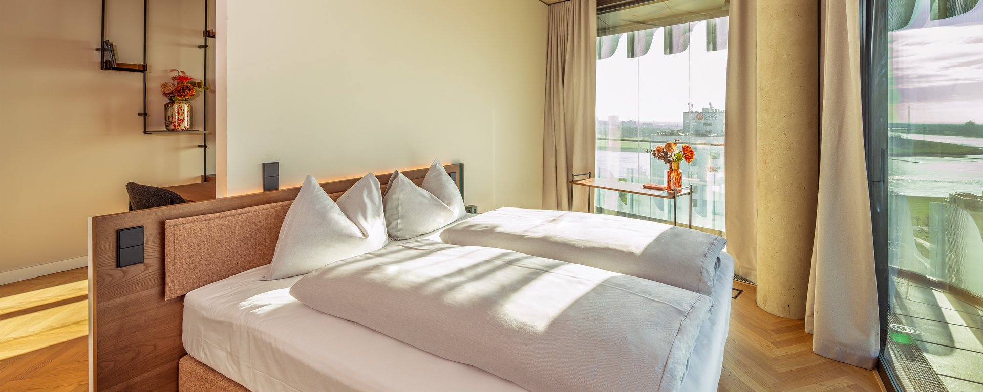 Schlafzimmer der Suite Loggia mit Doppelbett und bodentiefen Fenstern, die viel Tageslicht hereinlassen.