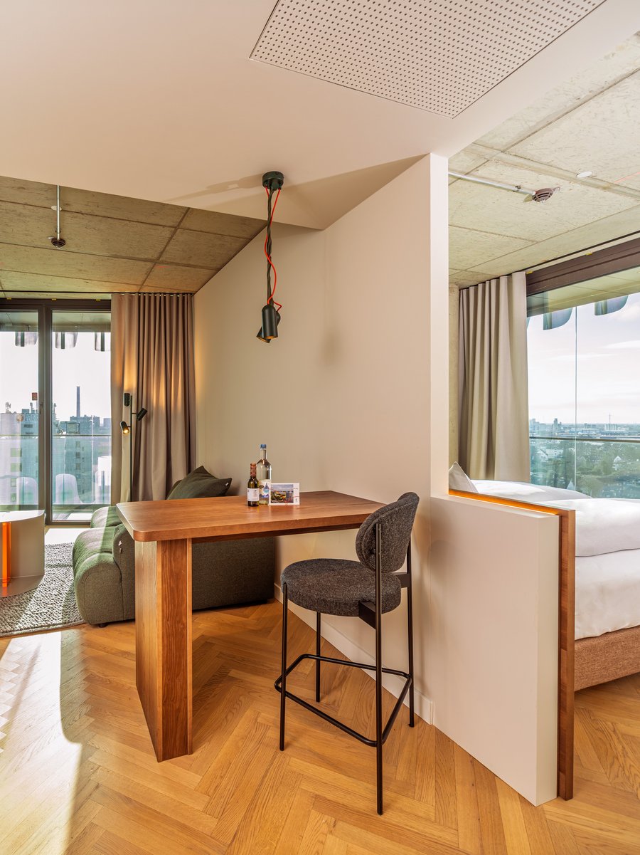 Blick durch den Wohnbereich auf die angrenzende Loggia mit Holztisch und Barhocker im The Zipper Hotel.