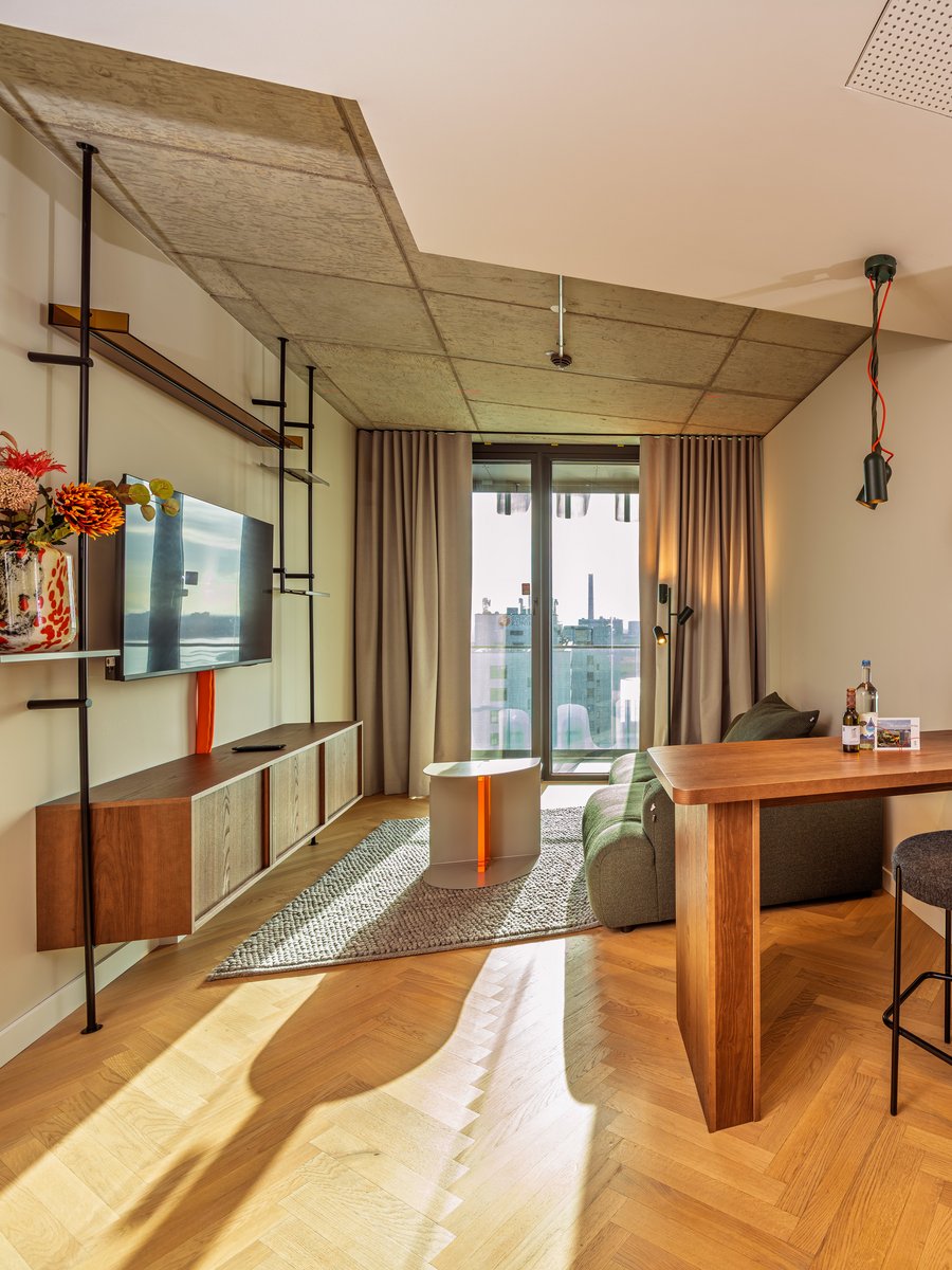 Blick durch den Wohnbereich auf die angrenzende Loggia mit Holztisch und Barhocker im The Zipper Hotel.
