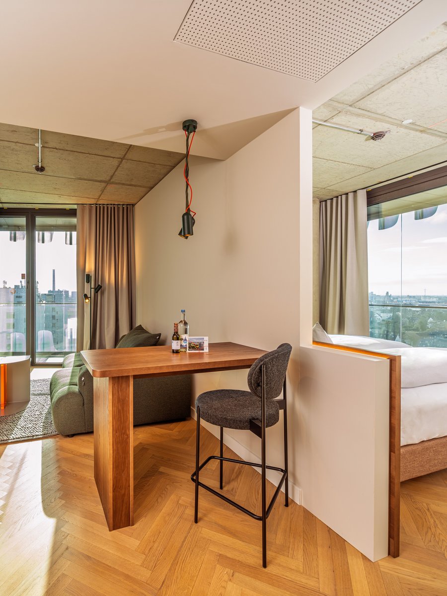 Blick durch den Wohnbereich auf die angrenzende Loggia mit Holztisch und Barhocker im The Zipper Hotel.