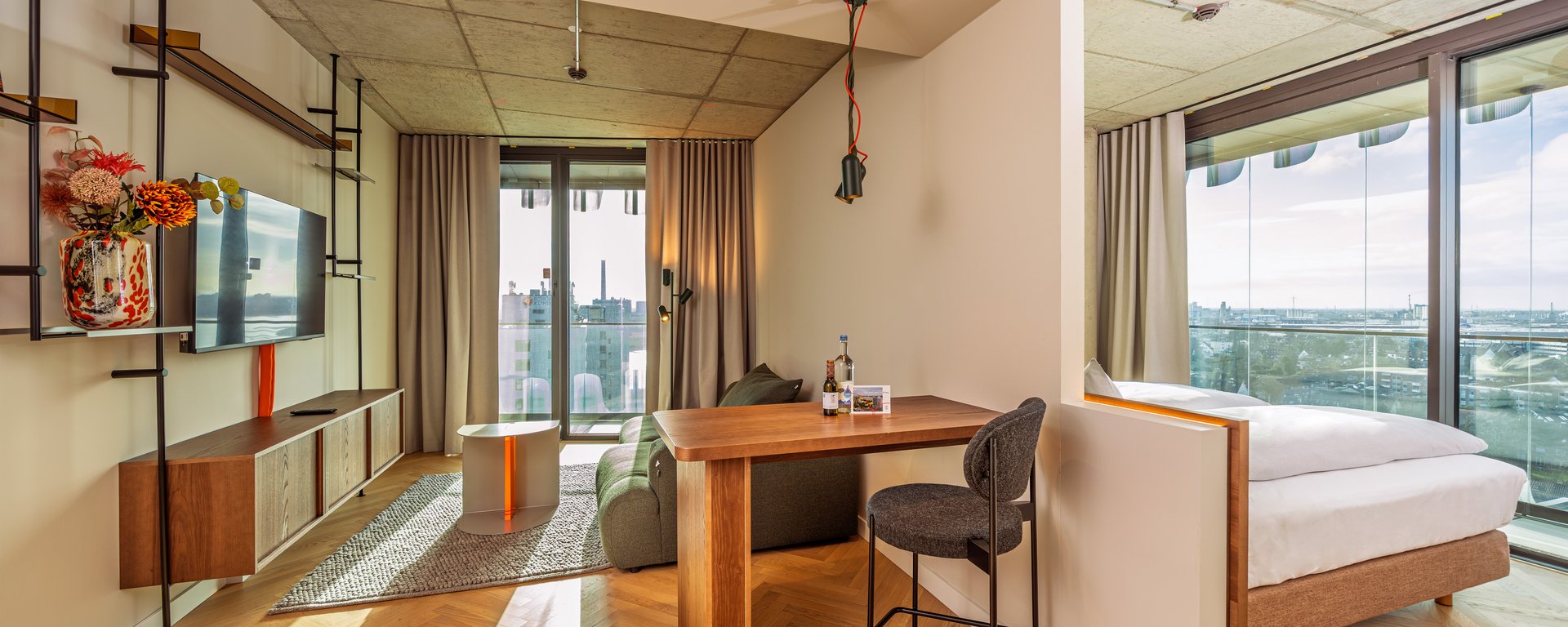 Blick durch den Wohnbereich auf die angrenzende Loggia mit Holztisch und Barhocker im The Zipper Hotel.