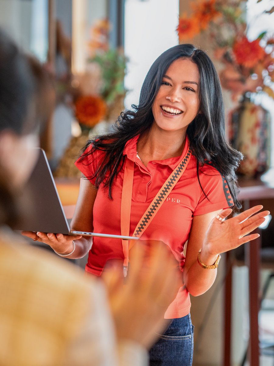 Eine Mitarbeiterin und eine Frau im karierten Blazer unterhalten sich angeregt in einer hellen Lounge-Atmosphäre