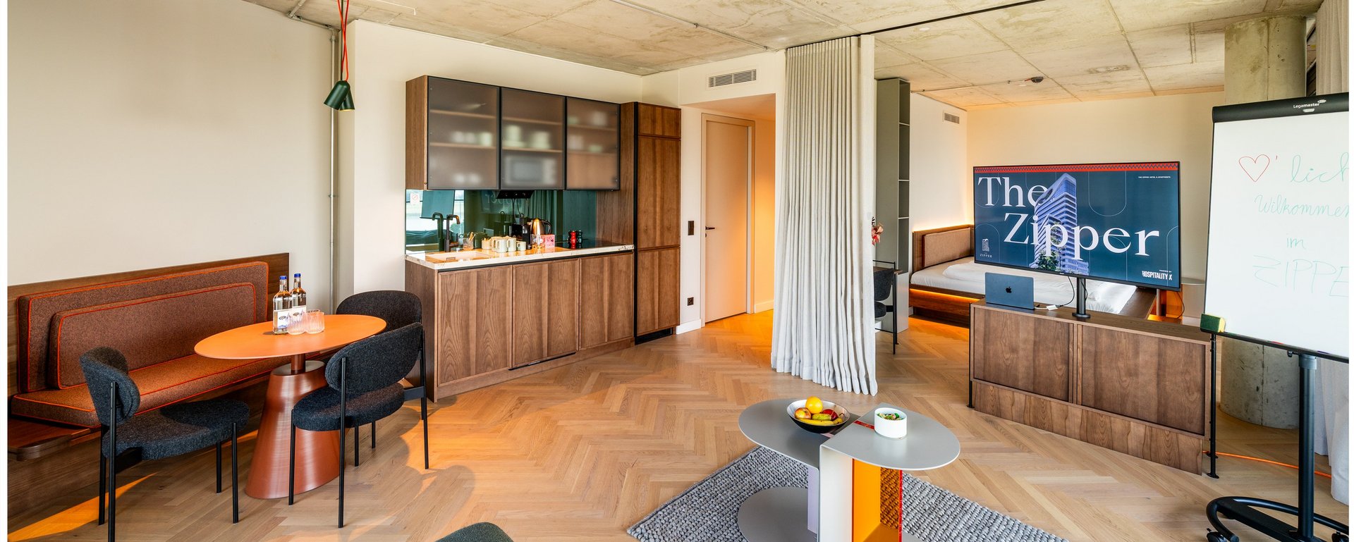 Moderne Hotelsuite mit Küchenzeile, Esstisch, Sofa und TV im THE ZIPPER Hotel Düsseldorf.