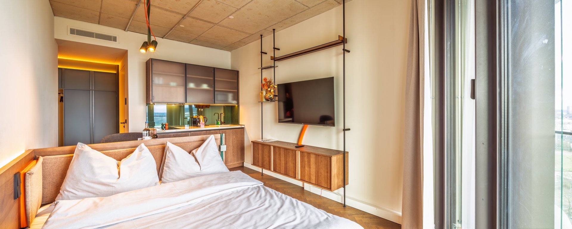 Schlafbereich im Apartment Skyline mit gemütlichem Doppelbett, Parkettboden und Blick auf den Flat-TV.