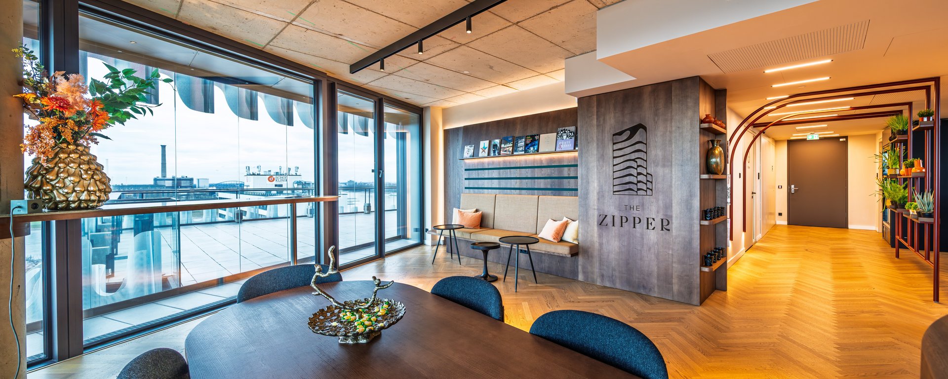 Lichtdurchfluteter Lounge-Bereich mit Konferenztisch und weitem Blick durch die Fensterfront auf die Umgebung.