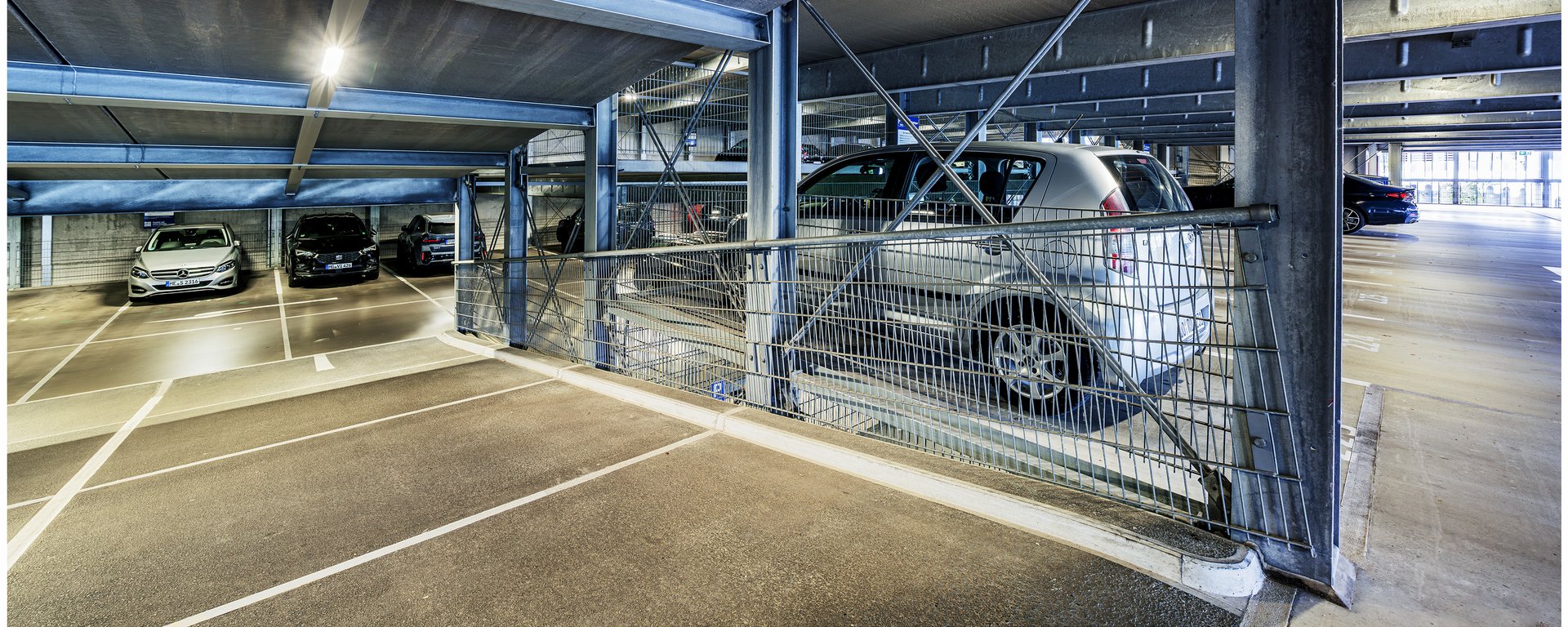 Innenansicht eines modernen Parkhauses mit markierten Parkflächen und geparkten Fahrzeugen.
