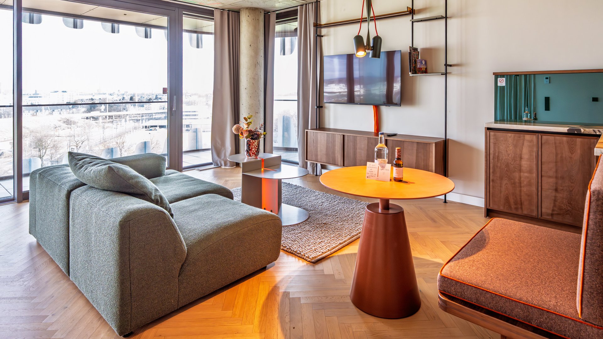 Wohnbereich im Apartment Home mit Blick auf die Fensterfront und minimalistisches Interieur.