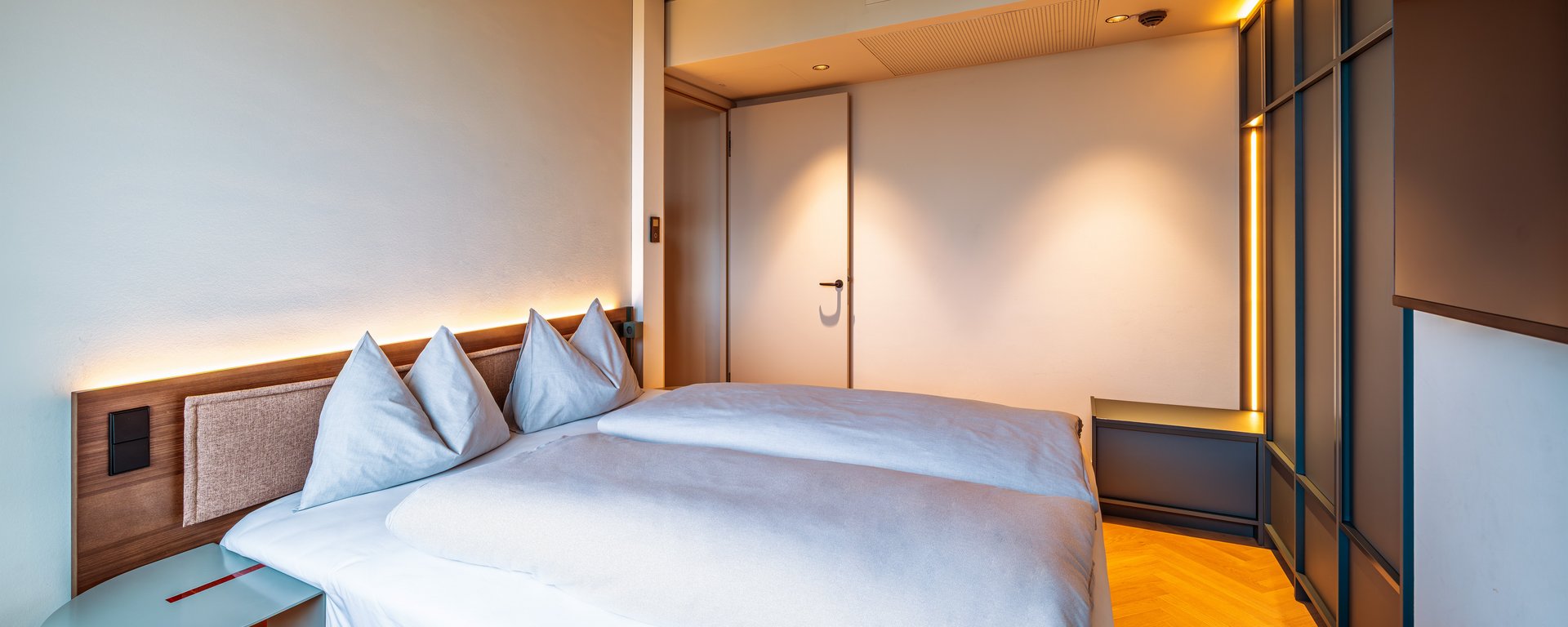 Gemütliches Doppelbett in der Suite mit indirekter Beleuchtung und Blick in das moderne Interieur.