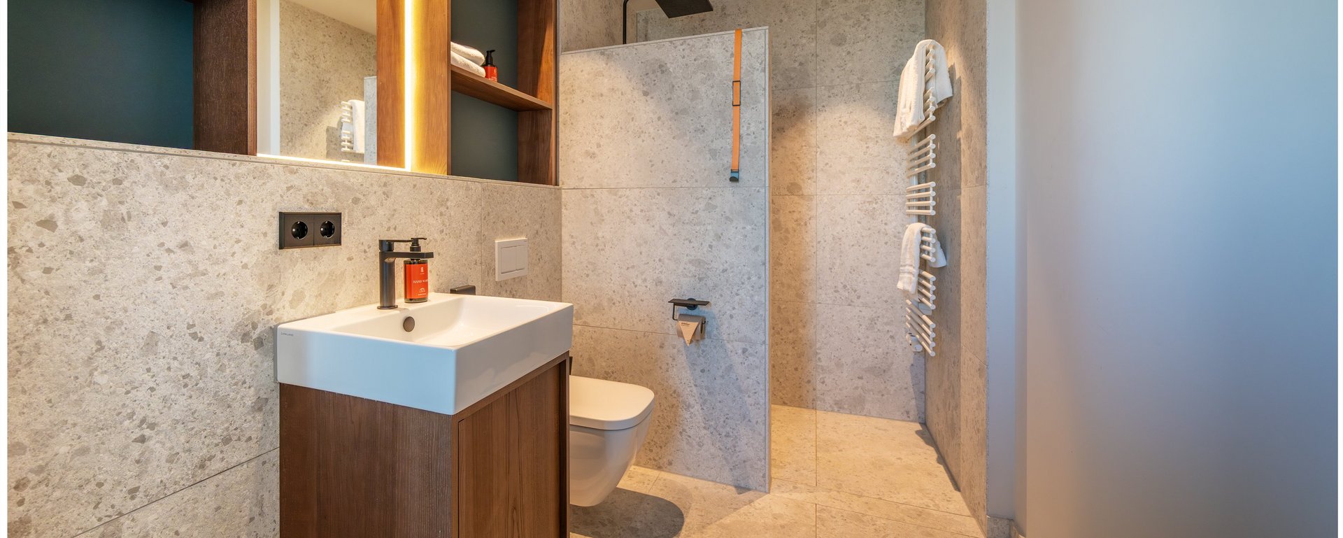 Modernes Hotelbadezimmer mit Waschtisch, beleuchtetem Spiegel und ebenerdiger Dusche im THE ZIPPER Hotel Düsseldorf.