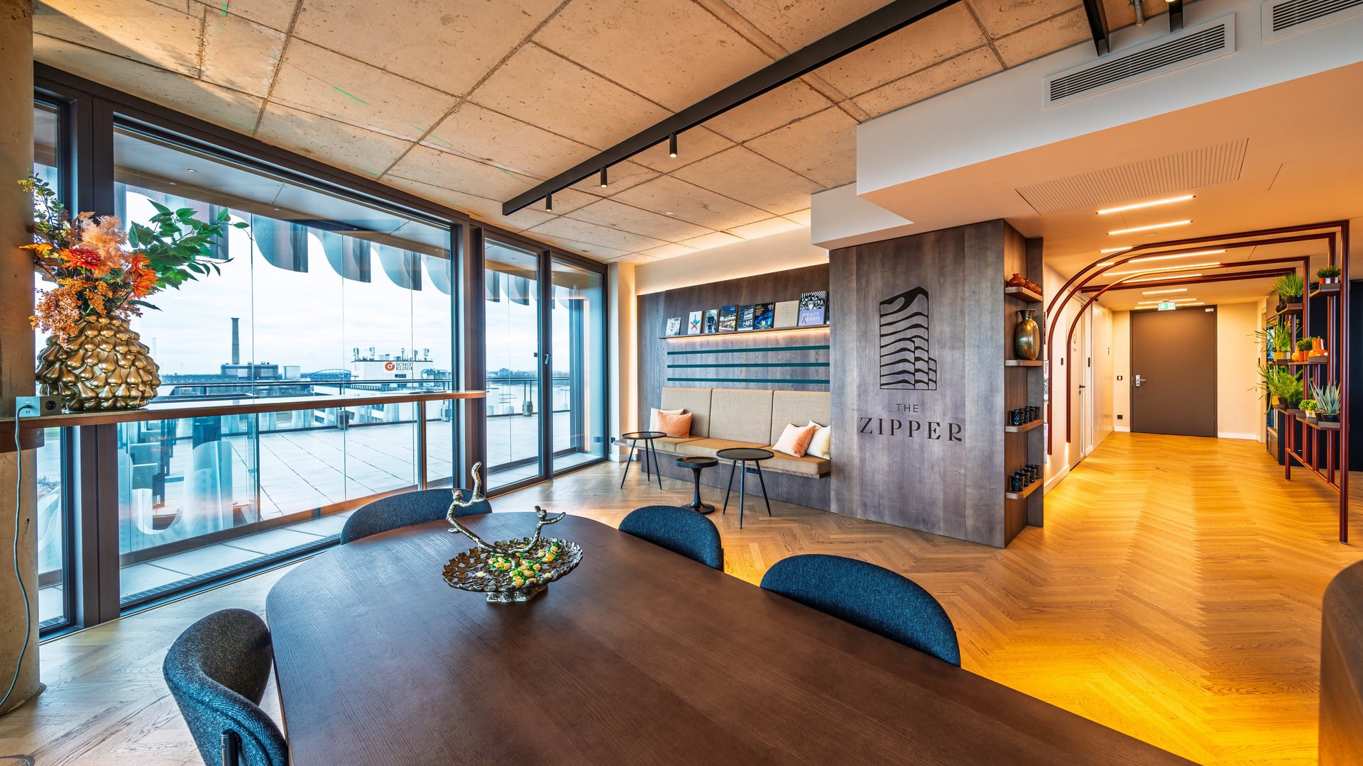 Lichtdurchfluteter Lounge-Bereich mit Konferenztisch und weitem Blick durch die Fensterfront auf die Umgebung.