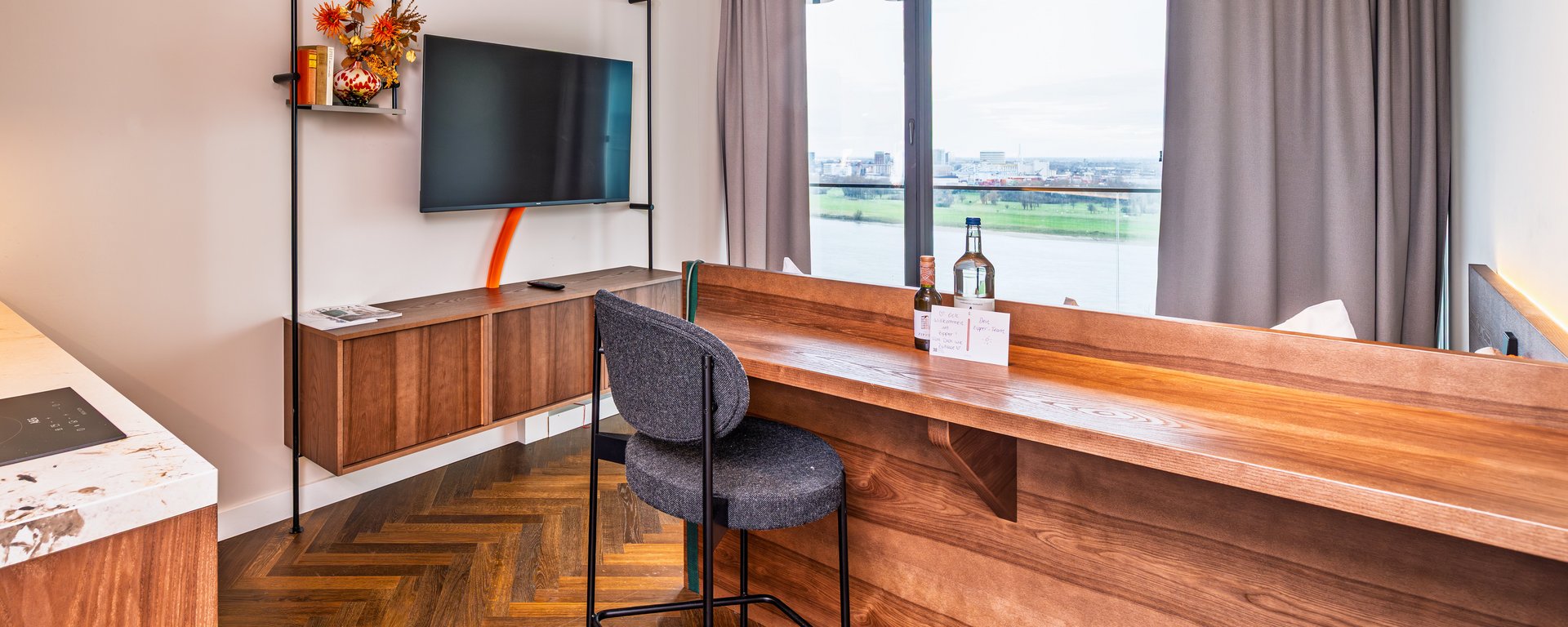 Kombinierter Wohn- und Arbeitsbereich im The Zipper mit hölzerner Bartheke, Barhocker und großem Fenster.