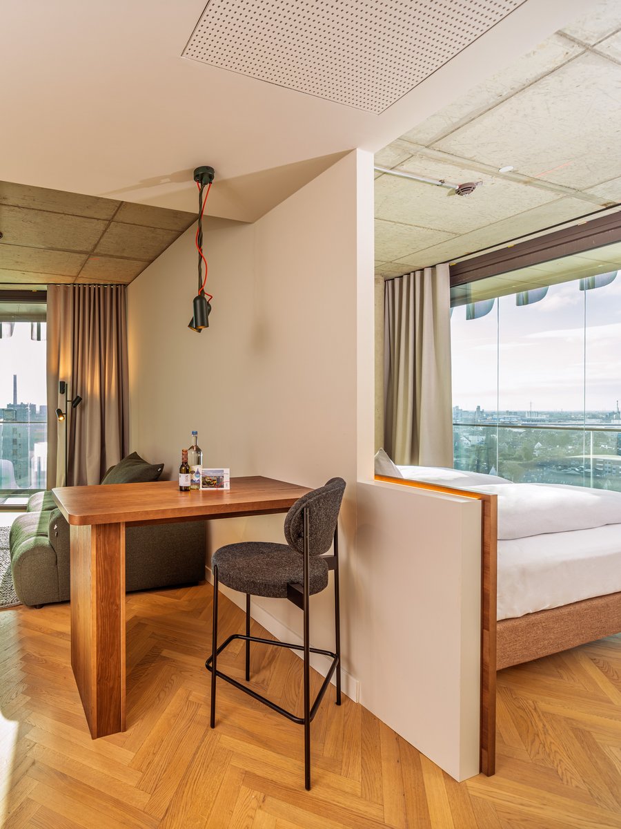 Blick durch den Wohnbereich auf die angrenzende Loggia mit Holztisch und Barhocker im The Zipper Hotel.