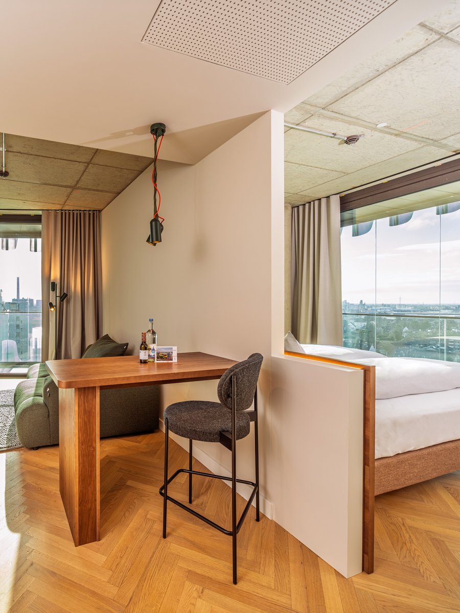 Blick durch den Wohnbereich auf die angrenzende Loggia mit Holztisch und Barhocker im The Zipper Hotel.