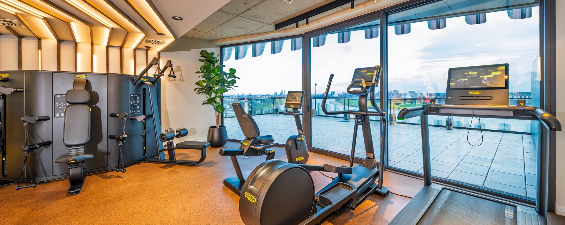 Modernes Gym im The Zipper Hotel mit Cardio-Geräten, Laufband und bodentiefen Fenstern für Training mit Aussicht.