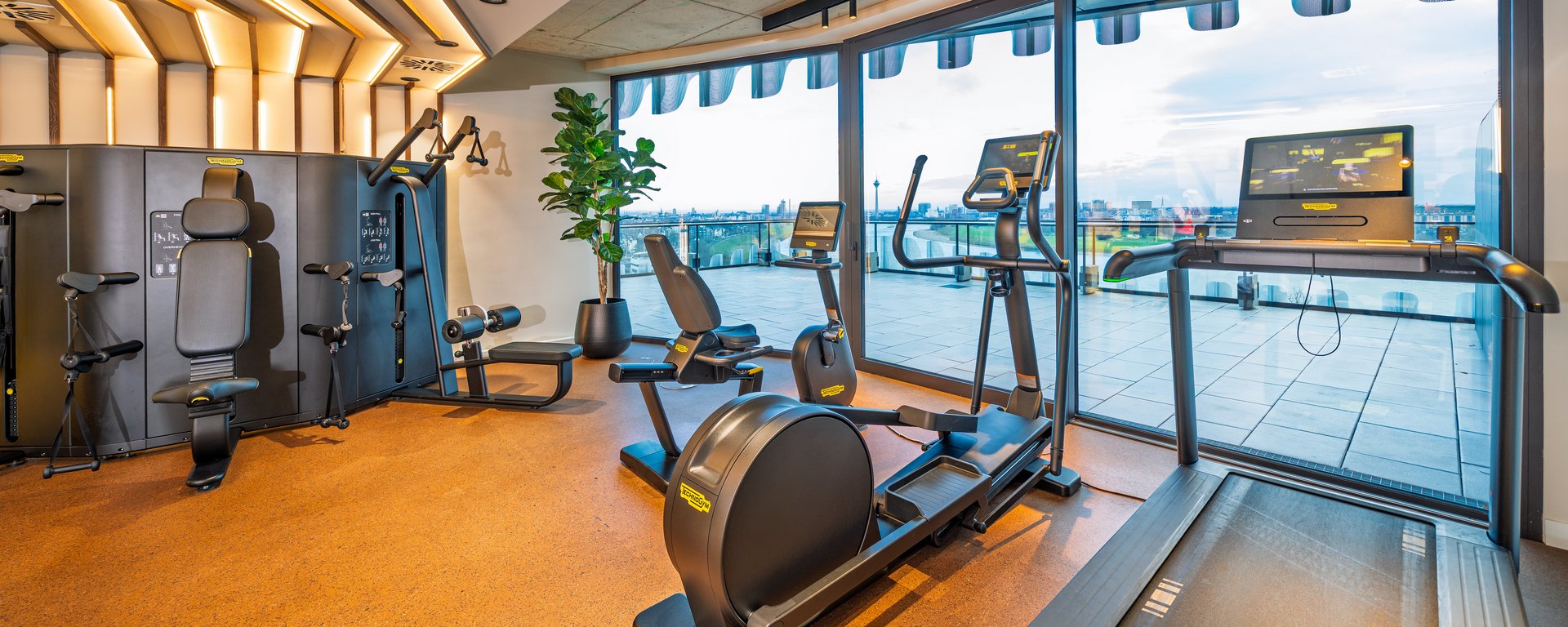 Modernes Gym im The Zipper Hotel mit Cardio-Geräten, Laufband und bodentiefen Fenstern für Training mit Aussicht.