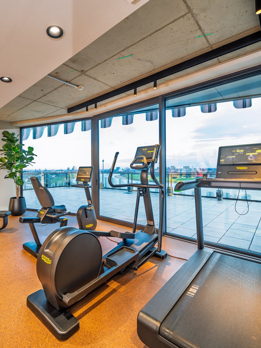 Modernes Gym im The Zipper Hotel mit Cardio-Geräten, Laufband und bodentiefen Fenstern für Training mit Aussicht.