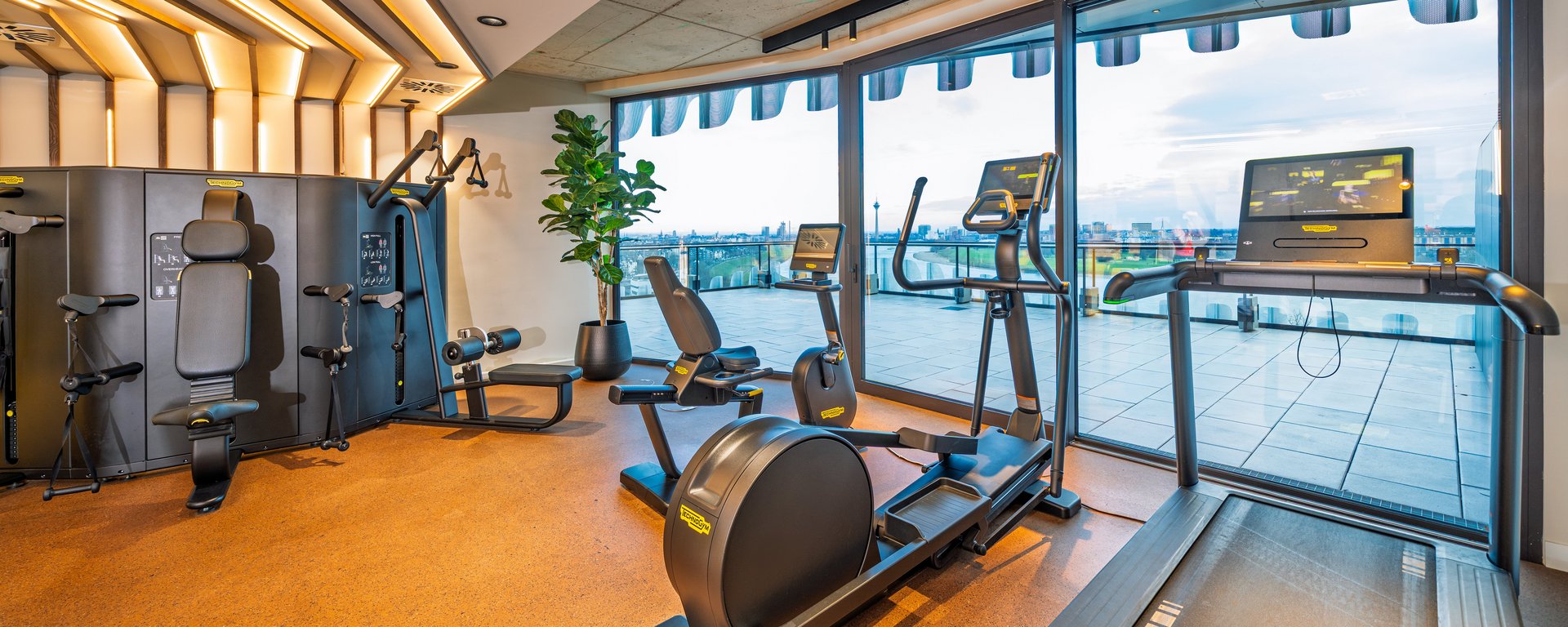 Modernes Gym im The Zipper Hotel mit Cardio-Geräten, Laufband und bodentiefen Fenstern für Training mit Aussicht.