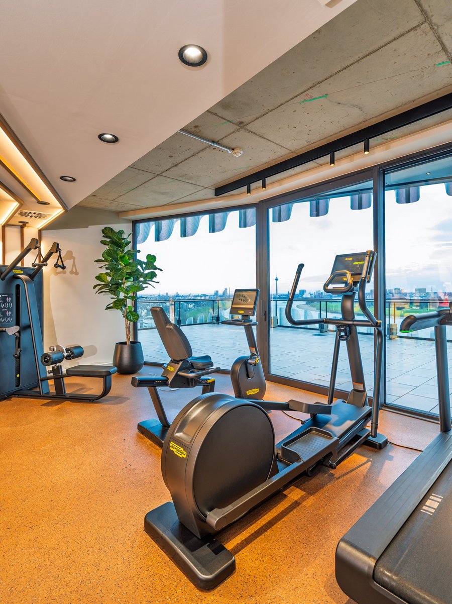 Modernes Gym im The Zipper Hotel mit Cardio-Geräten, Laufband und bodentiefen Fenstern für Training mit Aussicht.