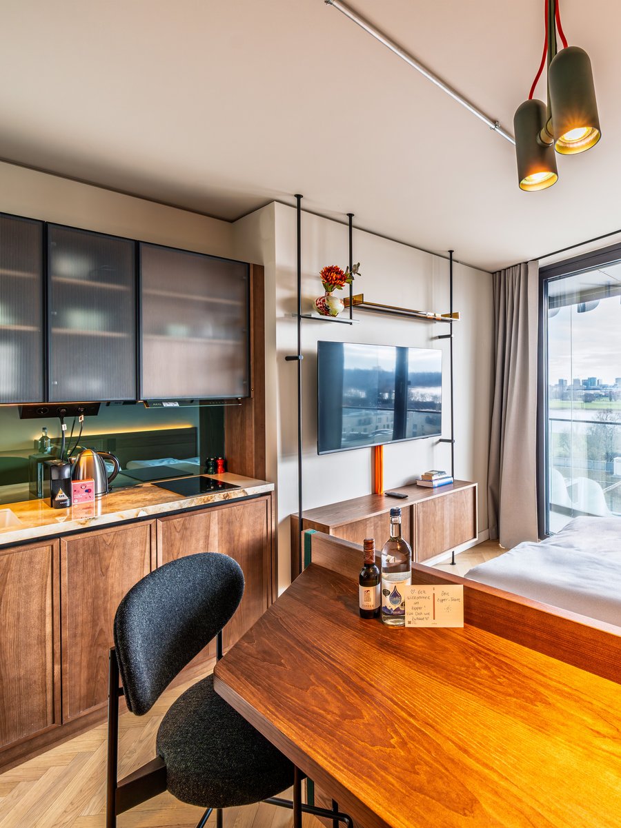 Modernes Apartment im The Zipper Hotel mit Holztisch, Kochnische und Blick auf das Bett sowie ein großes Fenster.