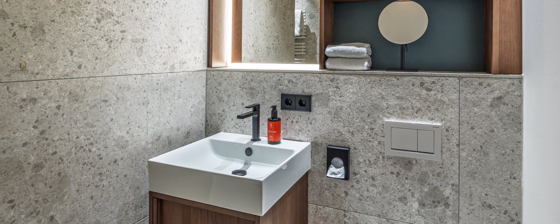 Kompakter Waschtisch im Badezimmer des Apartment Home Skyline mit Holzunterschrank und Spiegel.