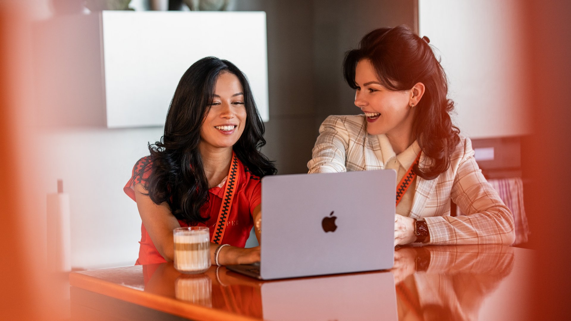 Zwei Frauen sitzen entspannt an einem Tisch mit einem MacBook