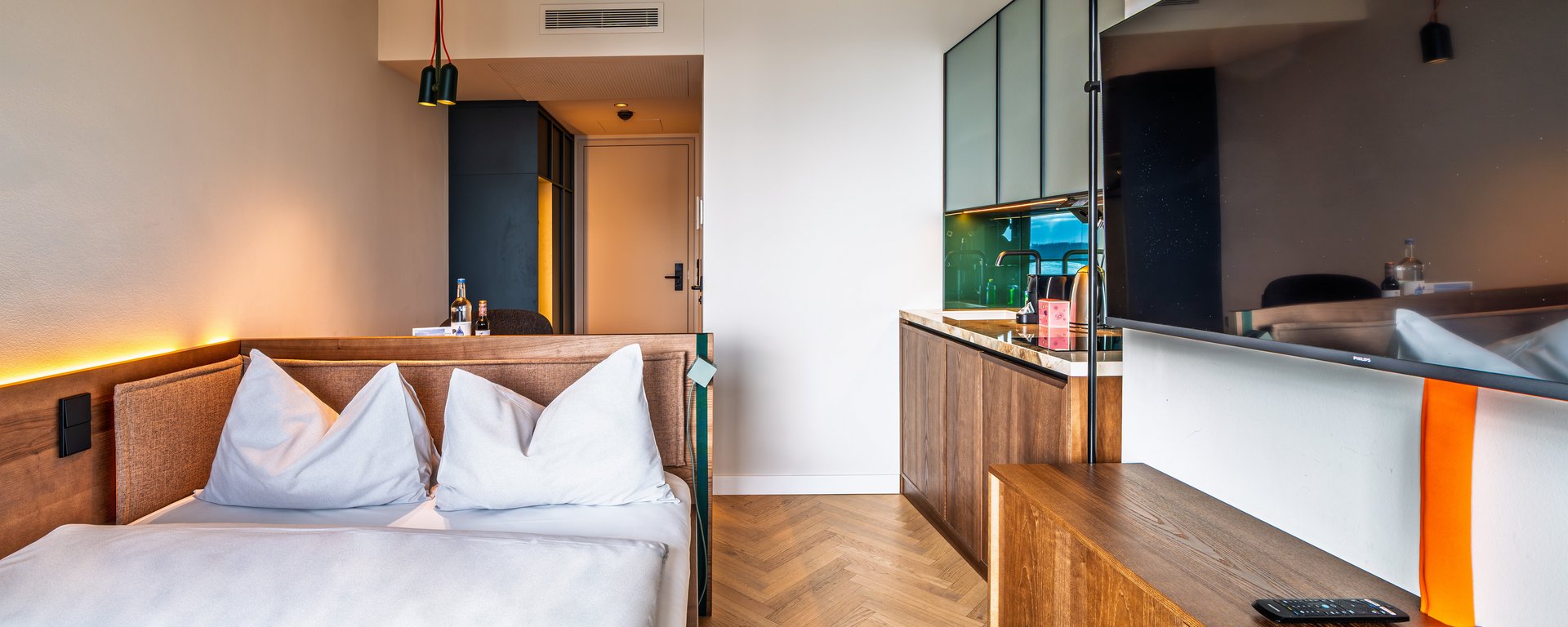 Perspektive vom Bett aus in das Apartment des The Zipper Hotels, inklusive TV-Wand und Einbauschränken aus Holz.